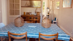 Un comedor con una mesa larga, dos cestas de mimbre, sillas de madera, un aparador de madera y una lámpara colgante.