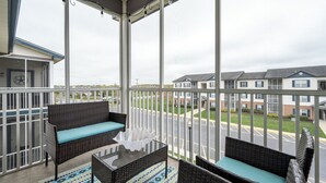 A balcony with wicker furniture, a glass table, and a view of a parking lot and buildings. - Villages of Five Points 3rd floor condo - great location & amenities! (Lewes)