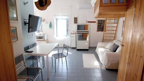 Een ruimtelijk ingerichte leefruimte met eethoek, een bank, een televisie en een kitchenette.