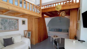Een loft-achtige kamer met een hoge nok, houten balken, een witte bank, een eettafel met stoelen en een grote kaart aan de muur.