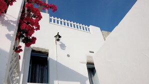 Een wit gebouw met een witte hek, een raam met verticale zonwering en een bloemenmand.