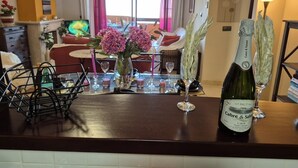 Habitación de hotel con zona de comedor, una botella de cava y un florero con flores sobre la encimera.
