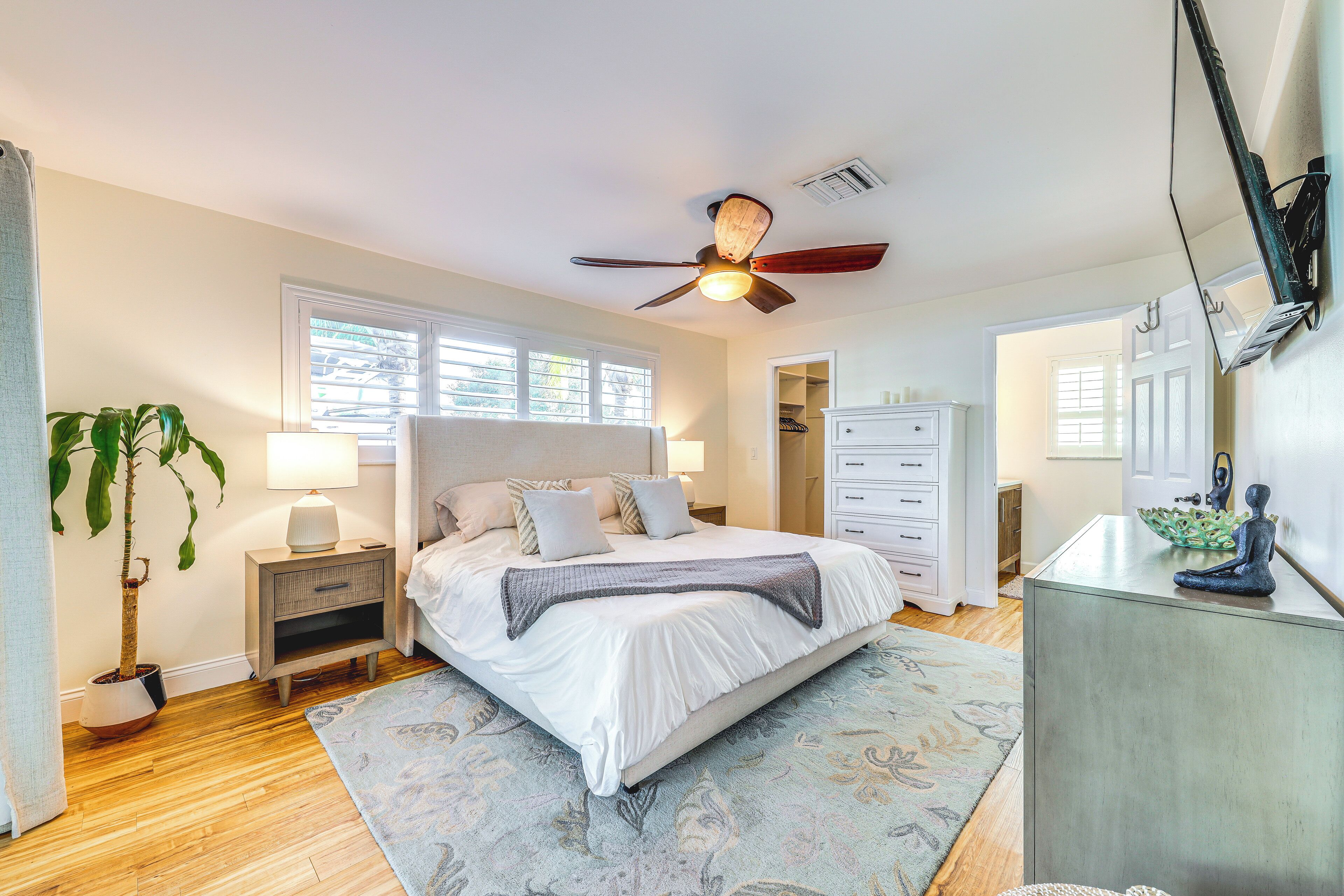 A bedroom with a bed, bedside tables, a ceiling fan, a nightstand, a potted plant, and a dresser.