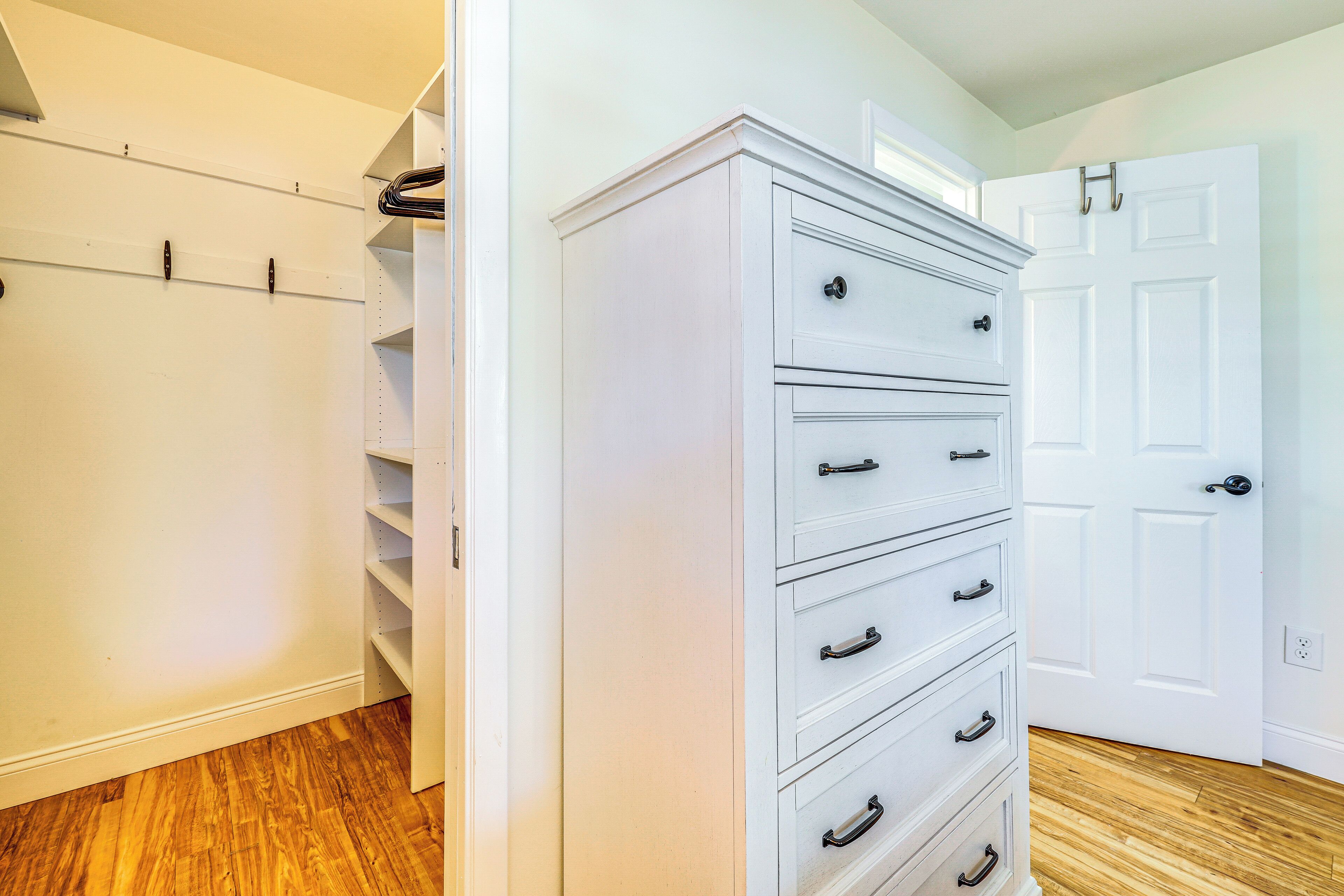 A walk-in closet with open shelves and a tall dresser with drawers.