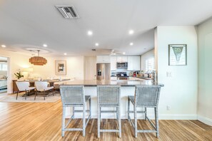 A spacious kitchen with a central island, white cabinetry, and a dining area with wicker chairs.