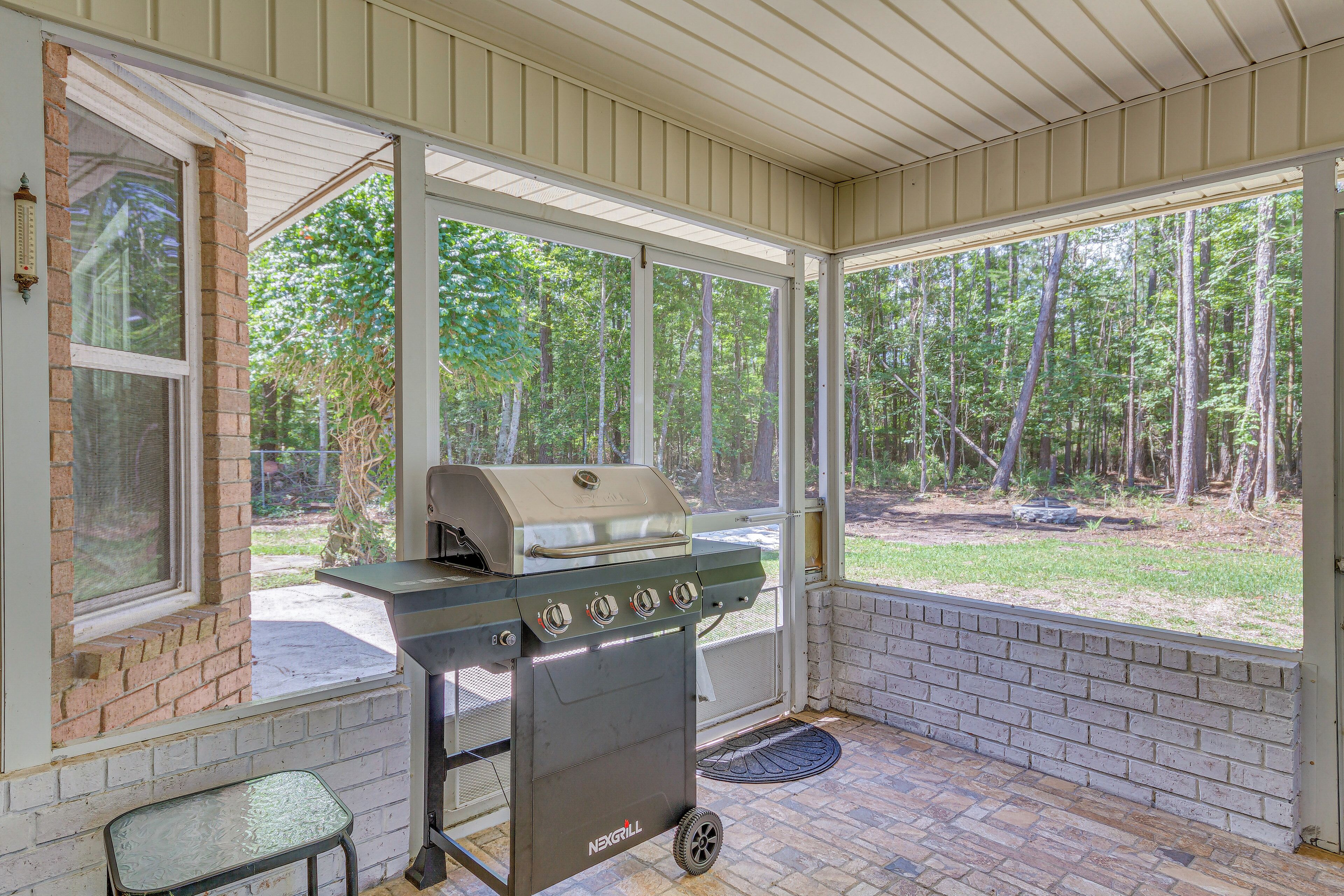 A covered outdoor area with a grill, a small table, and a view of a wooded area.