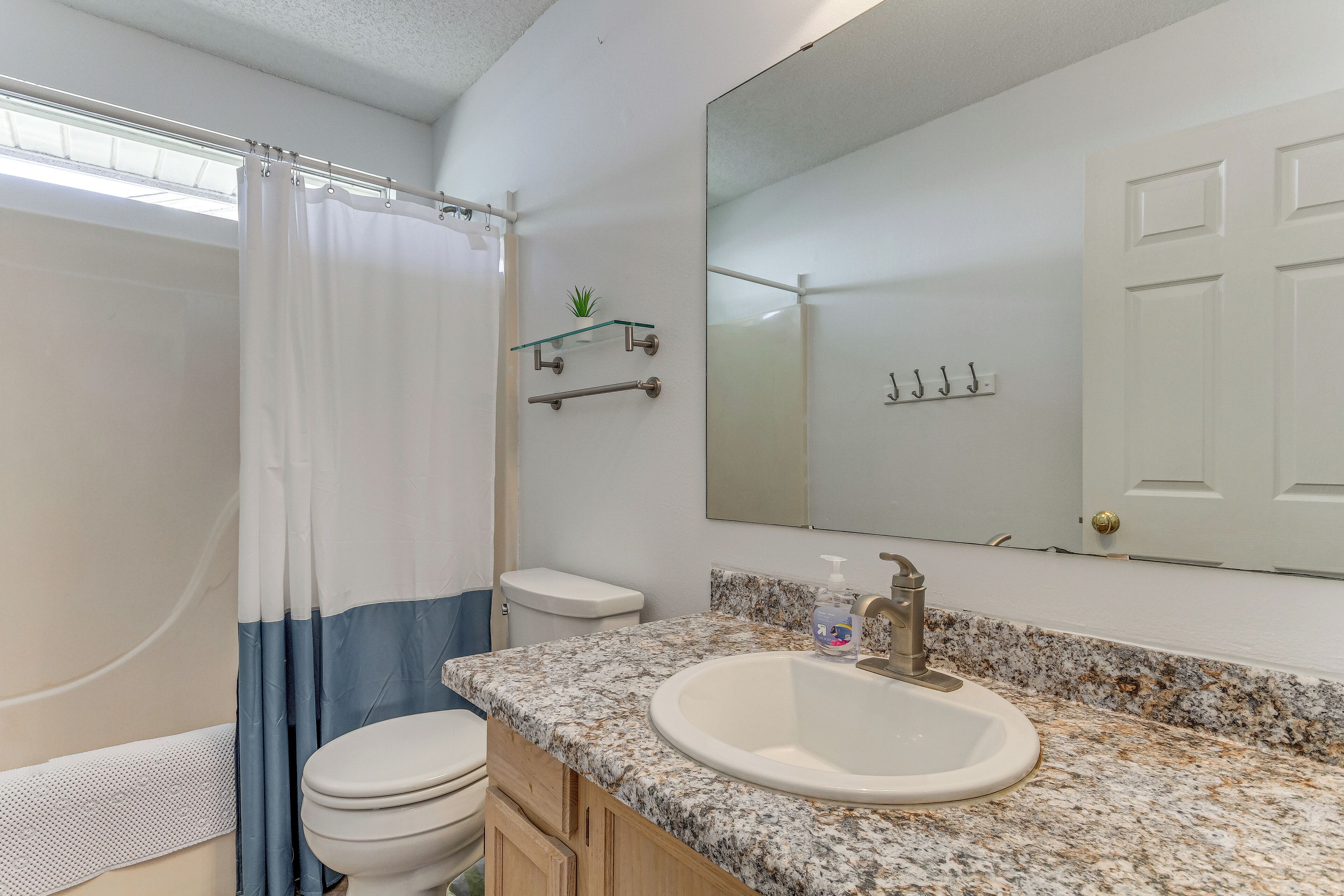 A bathroom with a shower, toilet, sink, and a large mirror.