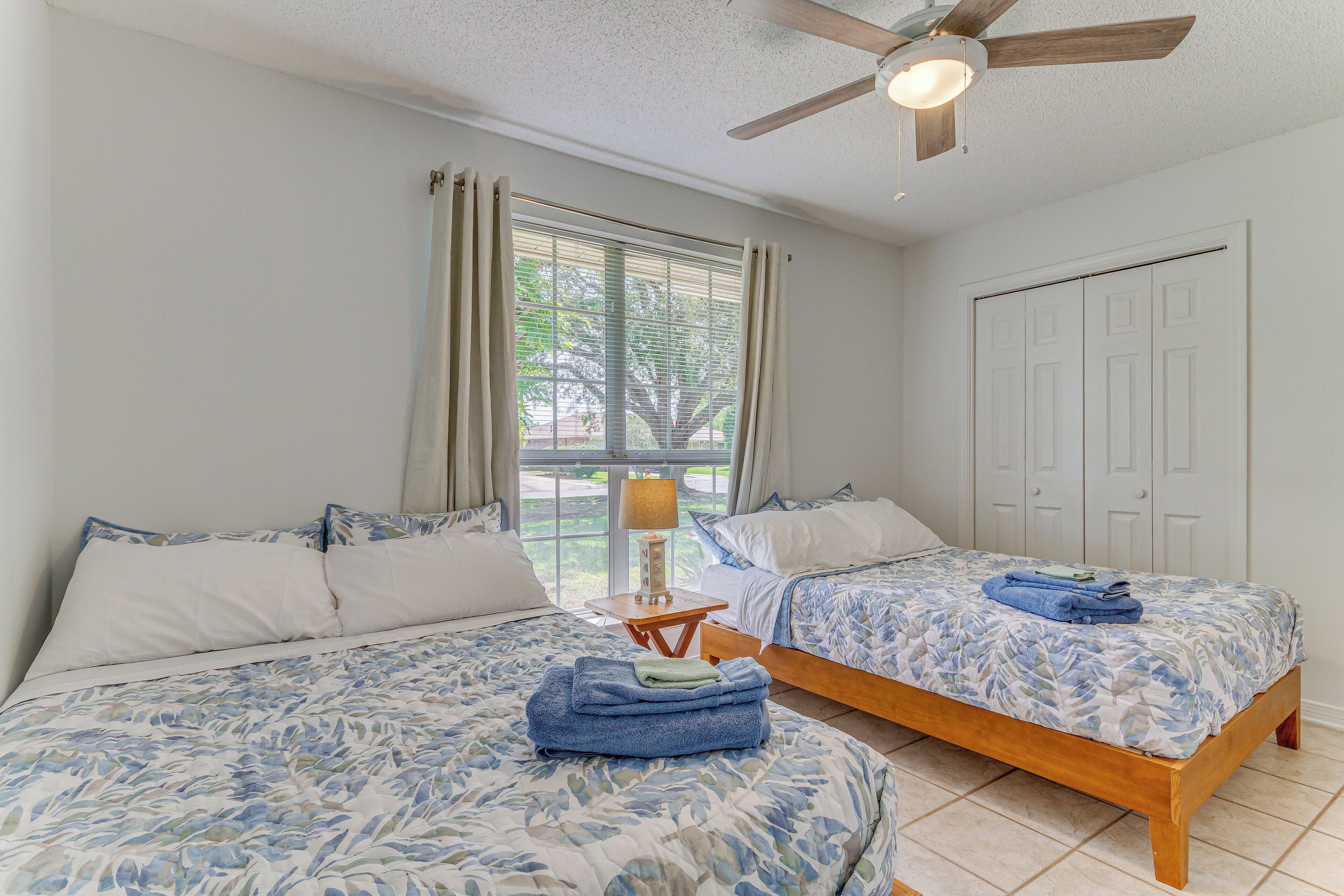 A bedroom with two beds, a ceiling fan, a window with curtains, and a door.
