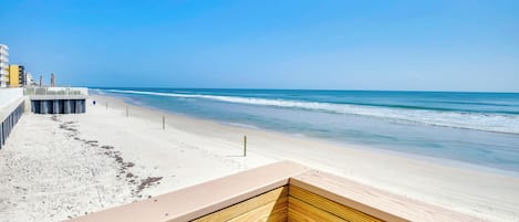 A beach view with a wooden deck and a pier in the background.