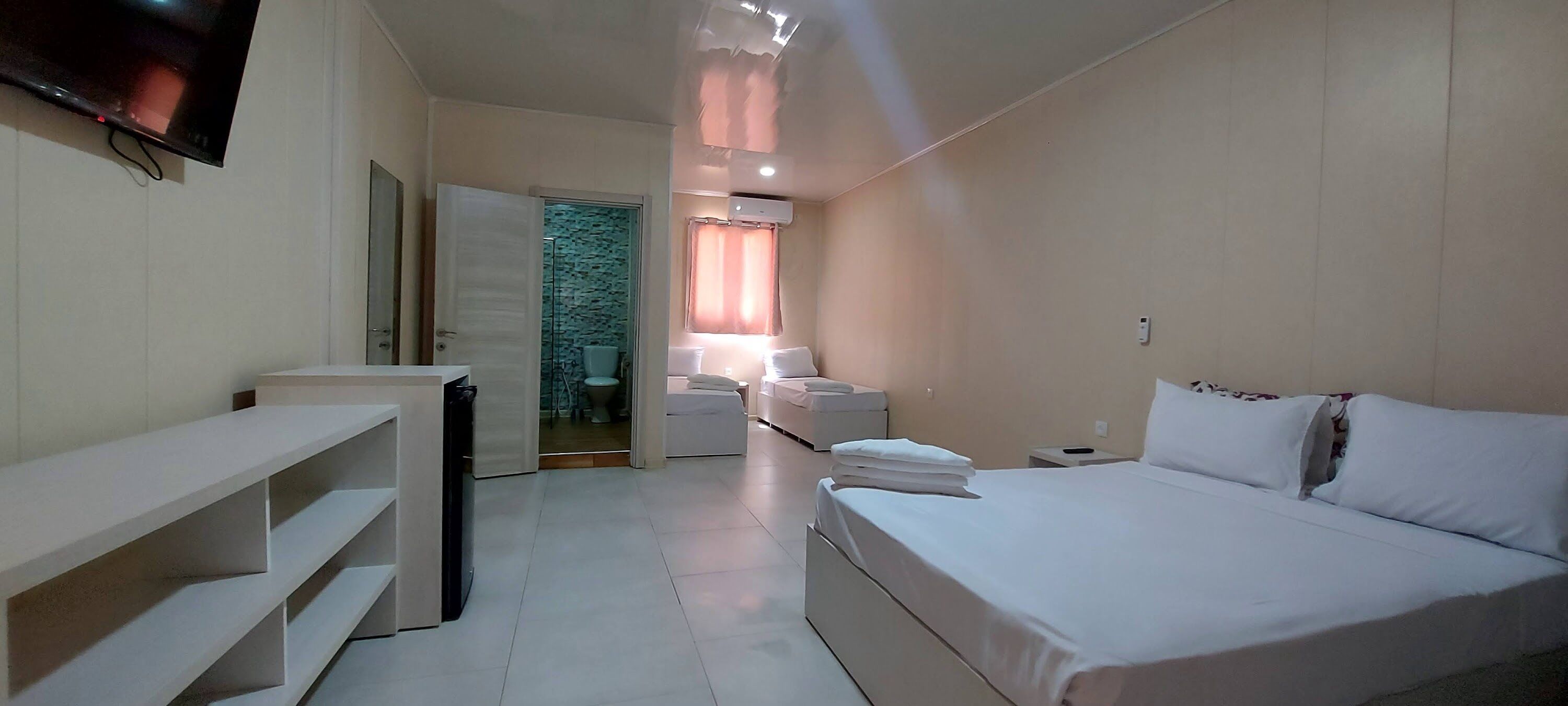 A modern hotel room with a large bed, a TV mounted on the wall, a small desk, and a bathroom visible through an open door.