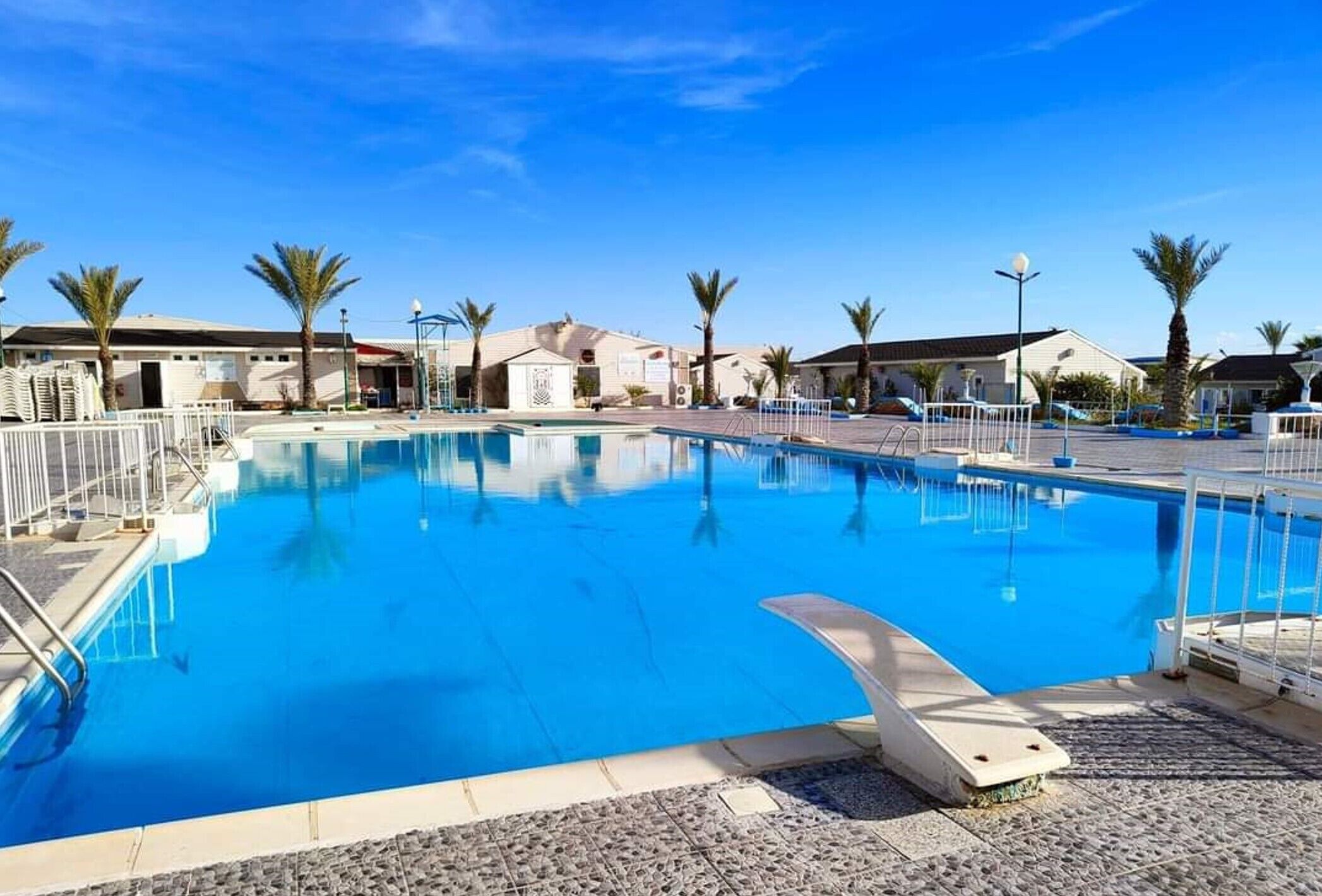 A swimming pool with a clear blue water, surrounded by palm trees and buildings.