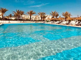 Una piscina azul cristalina con sillas de descanso y palmeras.