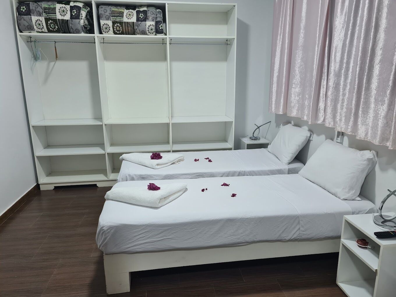 A hotel room with two beds, a wardrobe, and a bedside table.