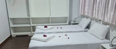 A hotel room with two beds, a wardrobe, and a bedside table.