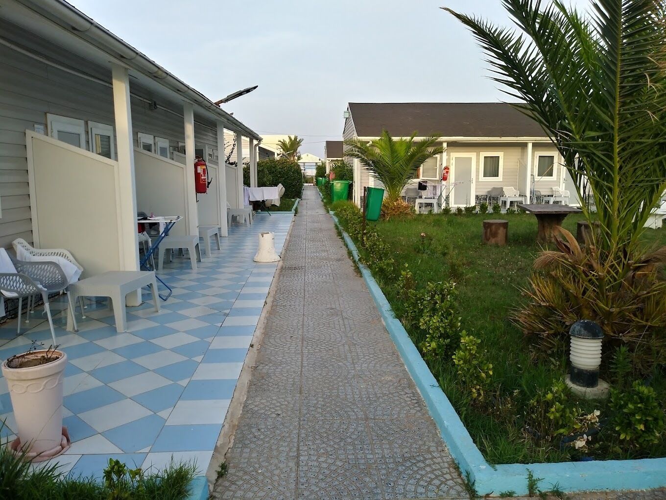 A corridor with a checkered floor leading to a building with outdoor seating and a small garden area.