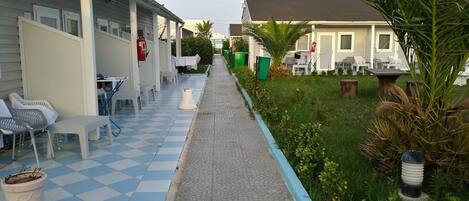 A corridor with a checkered floor leading to a building with outdoor seating and a small garden area.