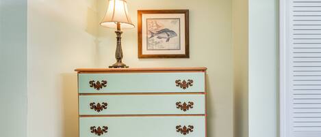 A light green dresser with ornate handles, a lamp, and a framed nautical illustration on the wall.
