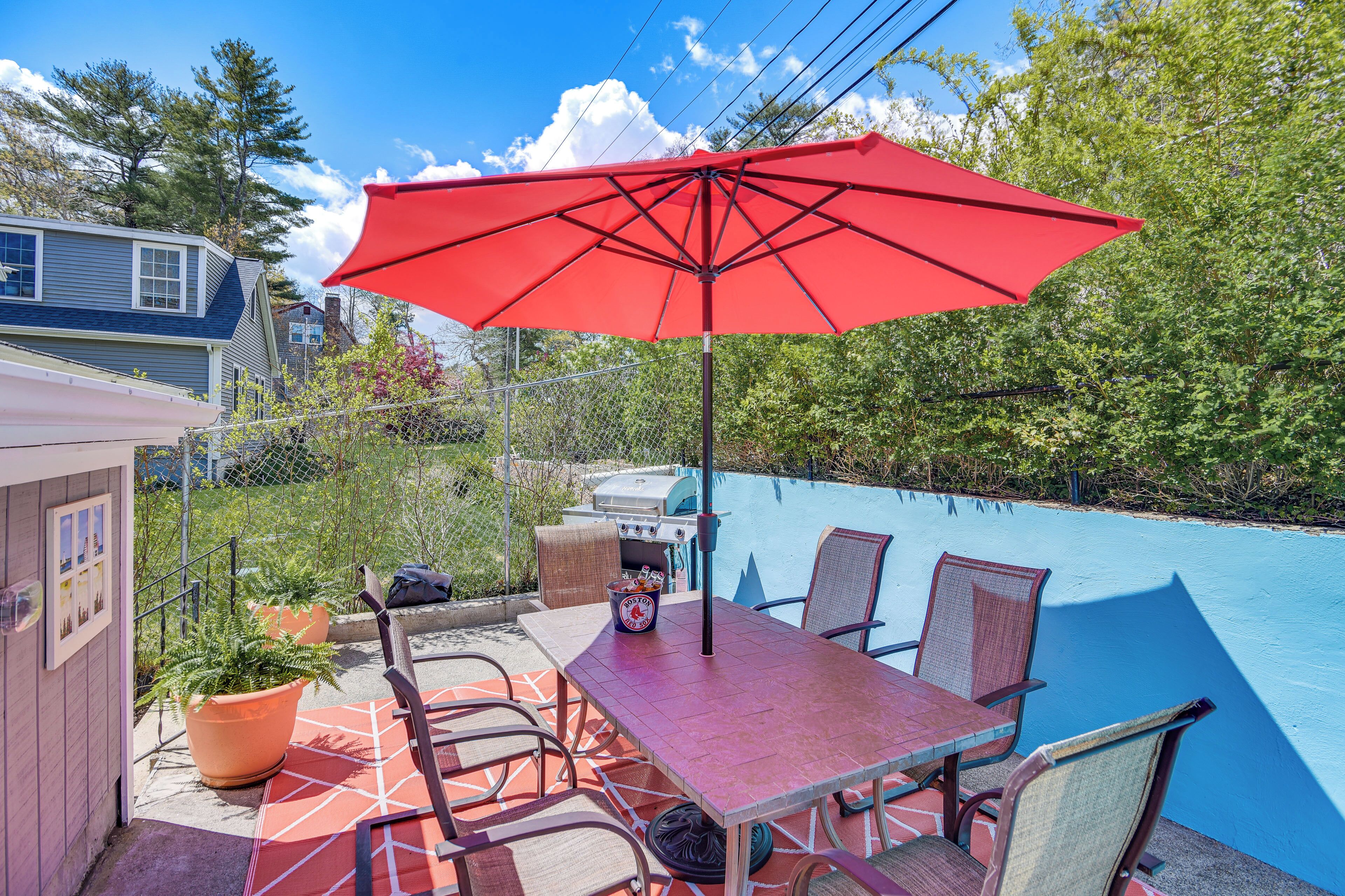 Eine Terrasse im Freien mit einem roten Sonnenschirm, einem Grill und einem Pool.