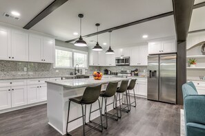 Uma cozinha moderna com armários brancos, bancada de granito, eletrodomésticos de aço inoxidável e banquetas.