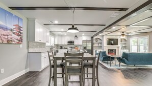 Een ruime keuken met witte kasten, een eethoek met tafel en stoelen, en een woonkamer met een bank en televisie.