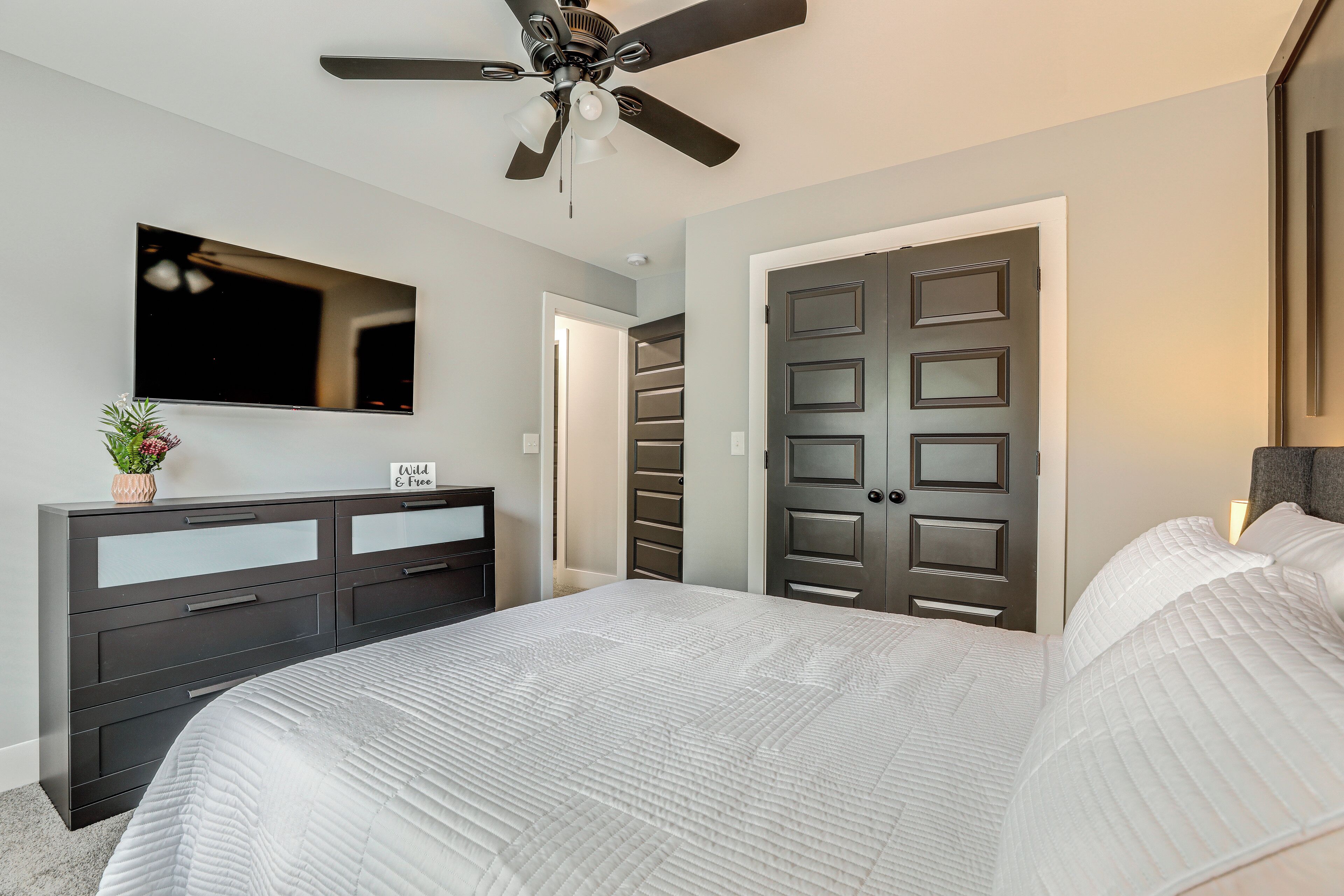 A bedroom with a bed, a dresser, a ceiling fan, a TV, and a door.