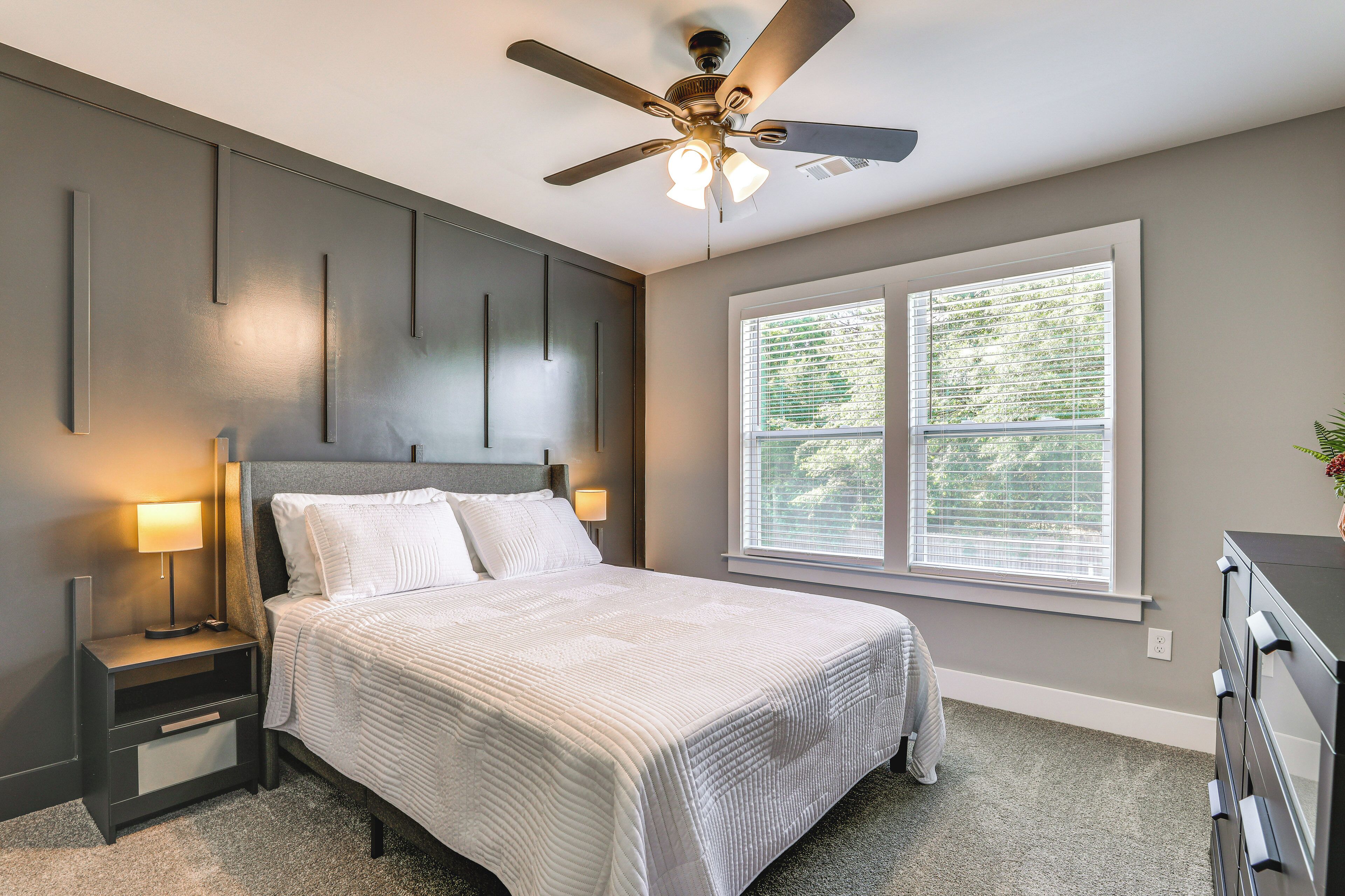 A bedroom with a bed, nightstands, a ceiling fan, a window with blinds, and a dresser.