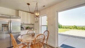 Una cocina con un refrigerador de acero inoxidable, sillas de madera, una mesa de comedor redonda y vistas al exterior a través de un vidrio.
