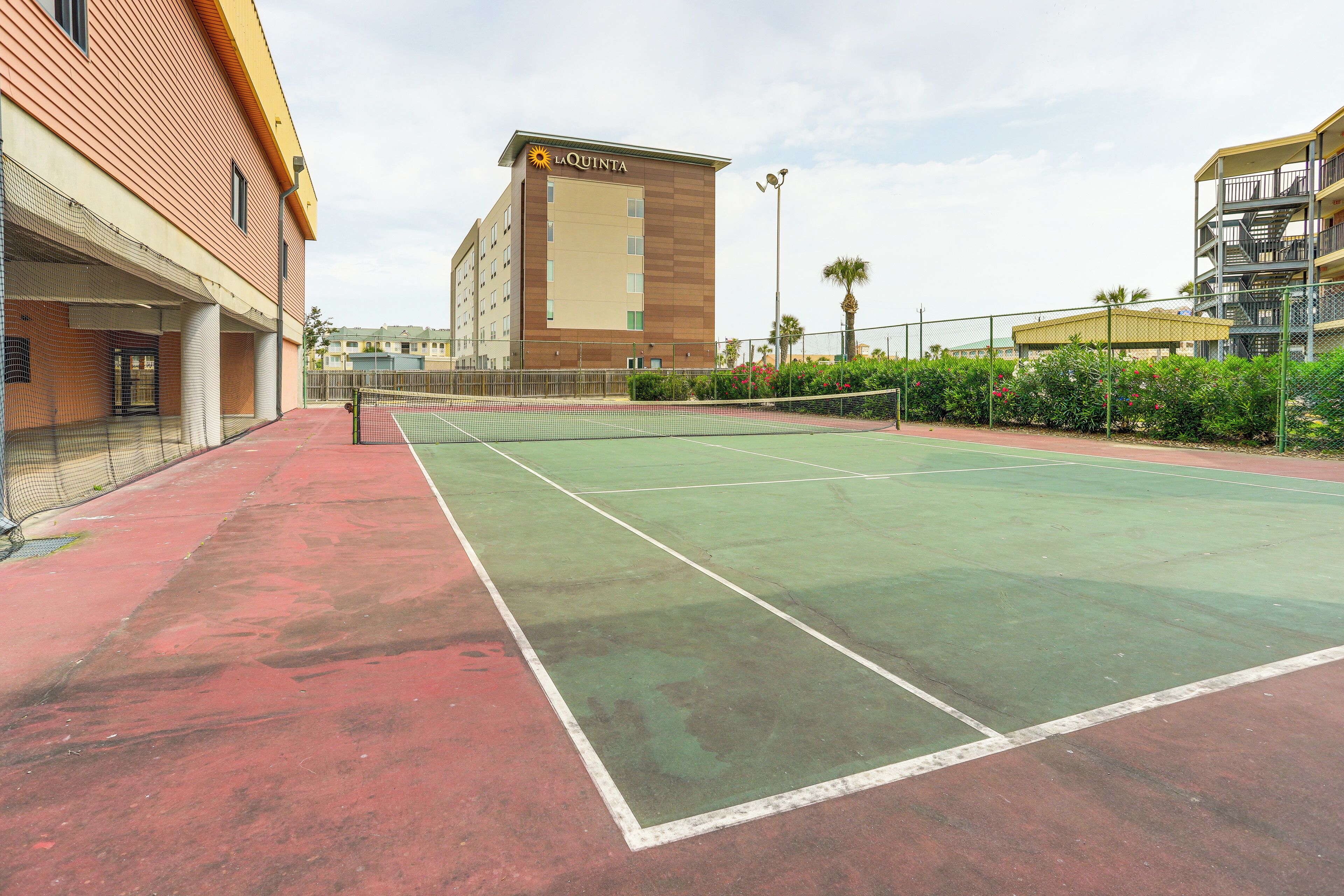 Un court de tennis extérieur, situé à côté d’un hôtel doté d’un toit plat et d’une enseigne indiquant « LAQUINTA ».