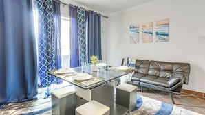 Un comedor moderno con una mesa de vidrio, cortinas azules y un sofá de cuero.