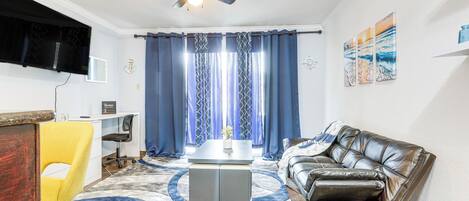 Ein Wohnzimmer mit Deckenventilator, einer Couch, einem Couchtisch und einem an der Wand befestigten Fernseher.
