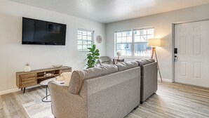 A living room with a sectional sofa, a flat-screen TV, a wooden cabinet, a desk, and a lamp. - Sarasota Duplex in Gillespie Park: 1 Mi to Dtwn! (Sarasota)