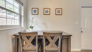 A dining area with a wooden table and chairs, a potted orchid, and three framed artworks on the wall. - Sarasota Duplex in Gillespie Park: 1 Mi to Dtwn! (Sarasota)