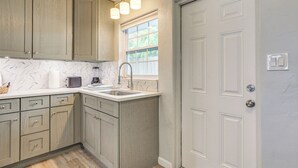 A kitchen with light wood cabinets, a white countertop, a sink, and a window with a view of greenery. - Sarasota Duplex in Gillespie Park: 1 Mi to Dtwn! (Sarasota)