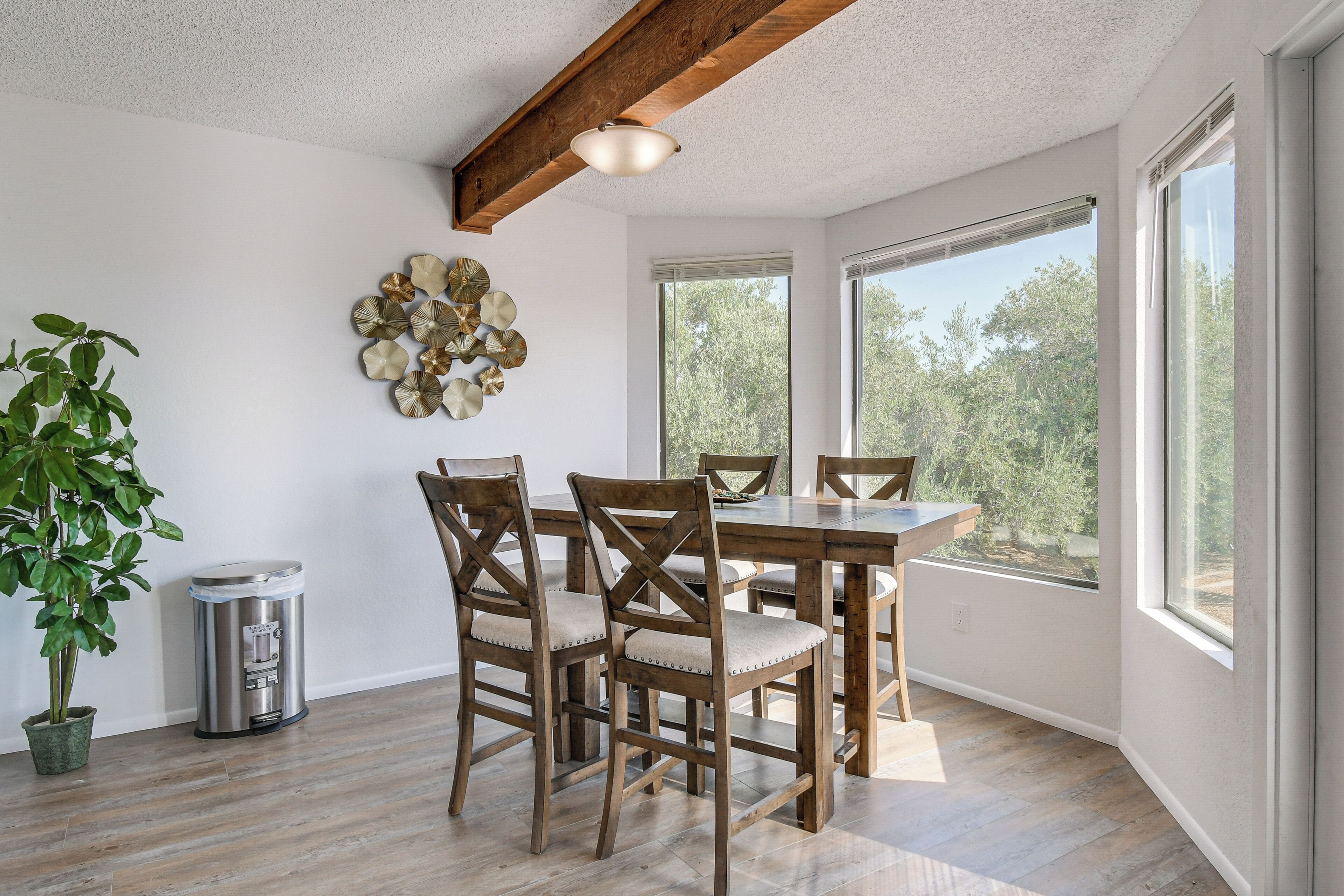 Un coin repas avec une table et des chaises en bois, une plante en pot et une poubelle.