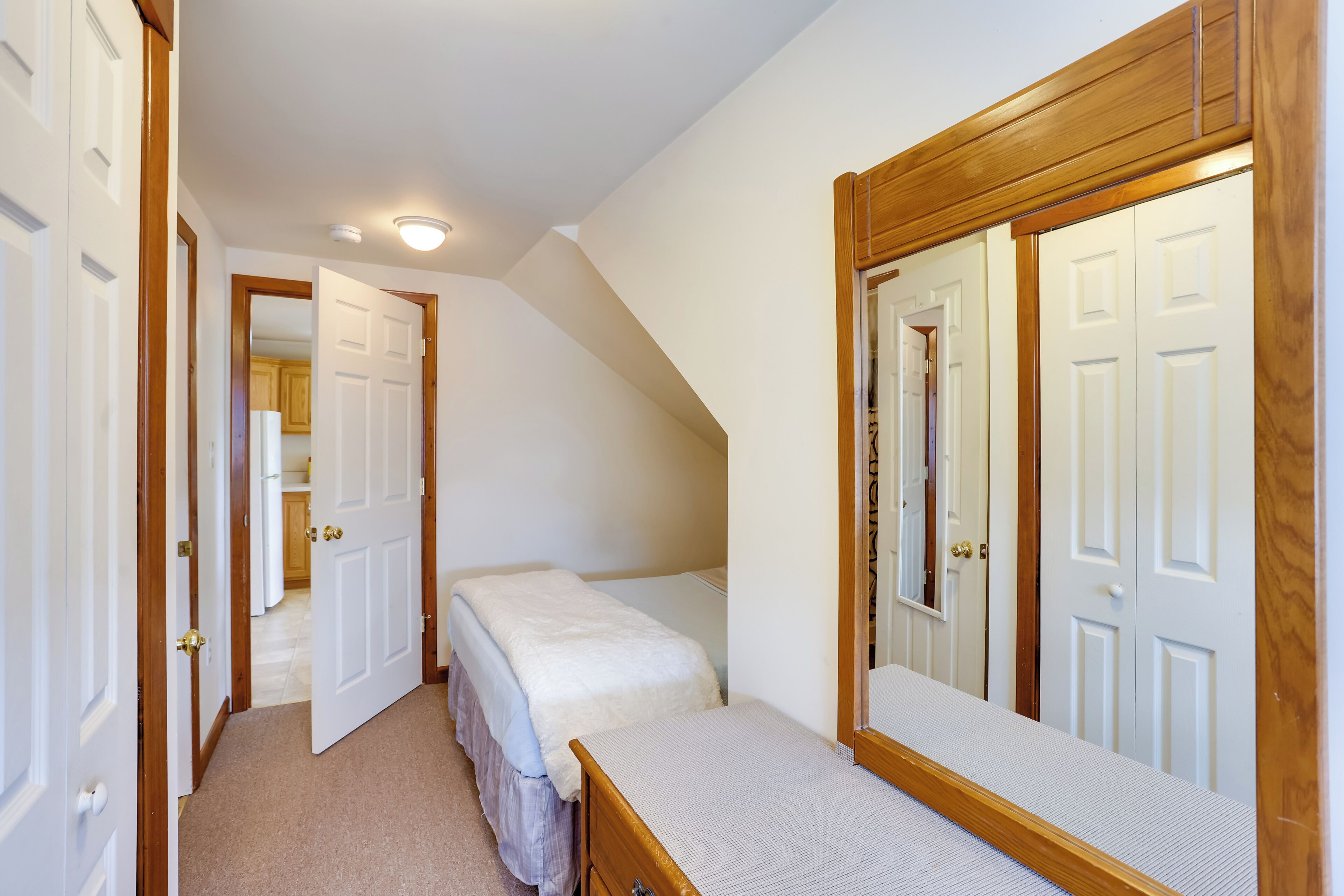 A bedroom with a single bed, a wooden dresser, a large mirror, and a closet with a wooden door.