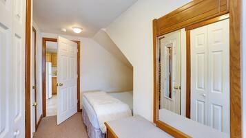 A bedroom with a single bed, a wooden dresser, a large mirror, and a closet with a wooden door.