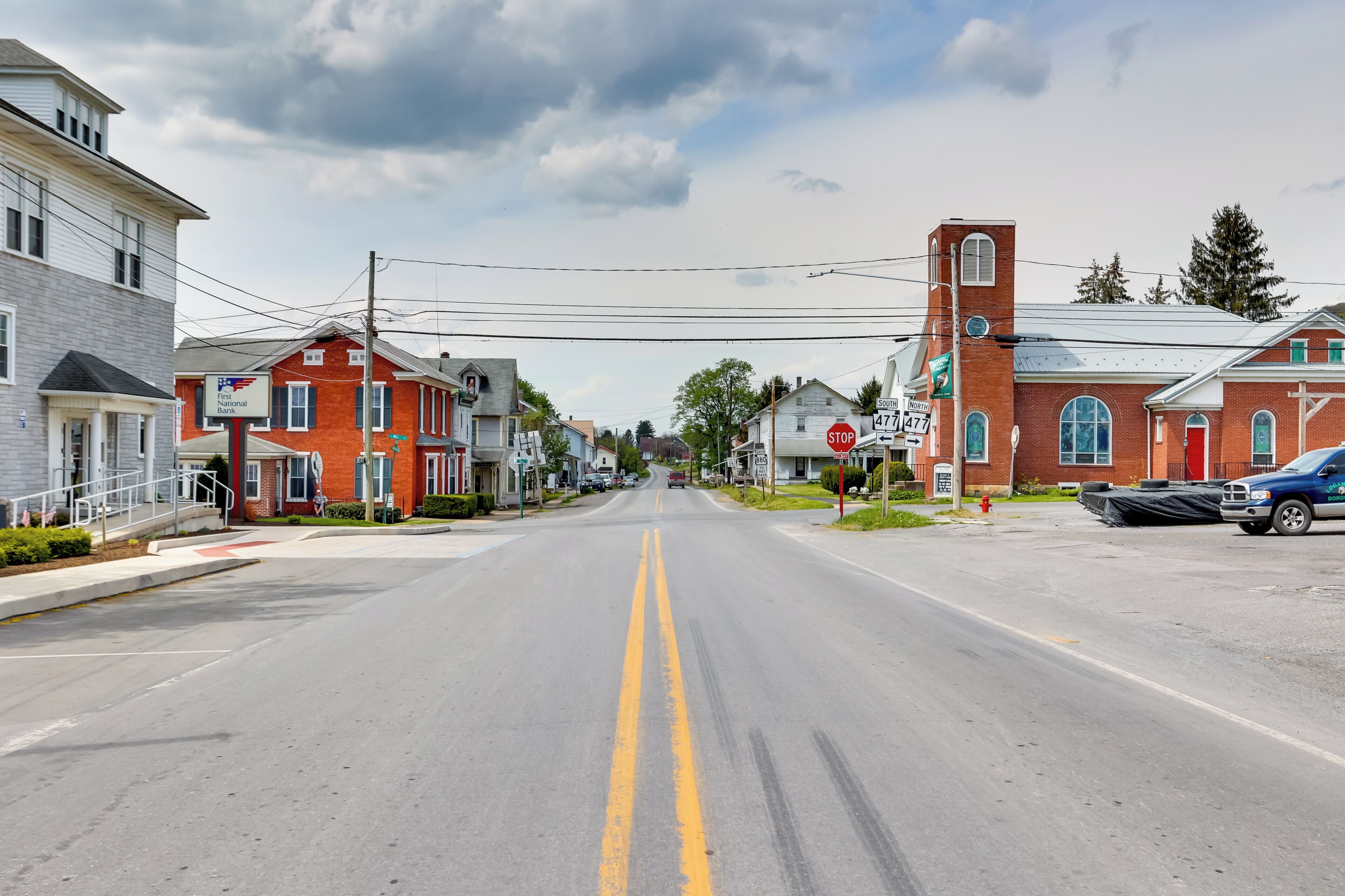 A street view with a red brick building, a white building, and a blue truck.