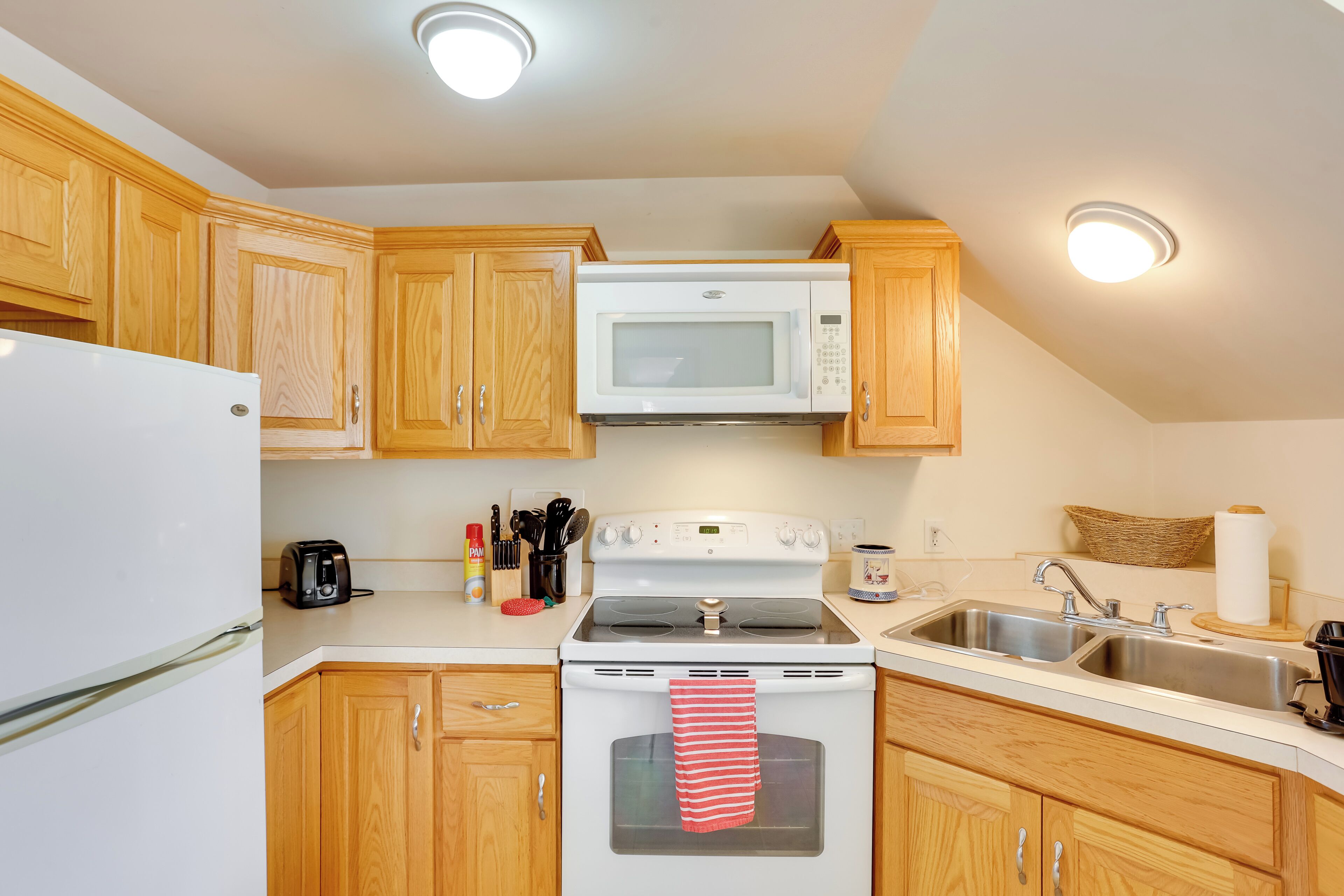 Una cocina con armarios de madera, un microondas blanco, una estufa y un refrigerador.