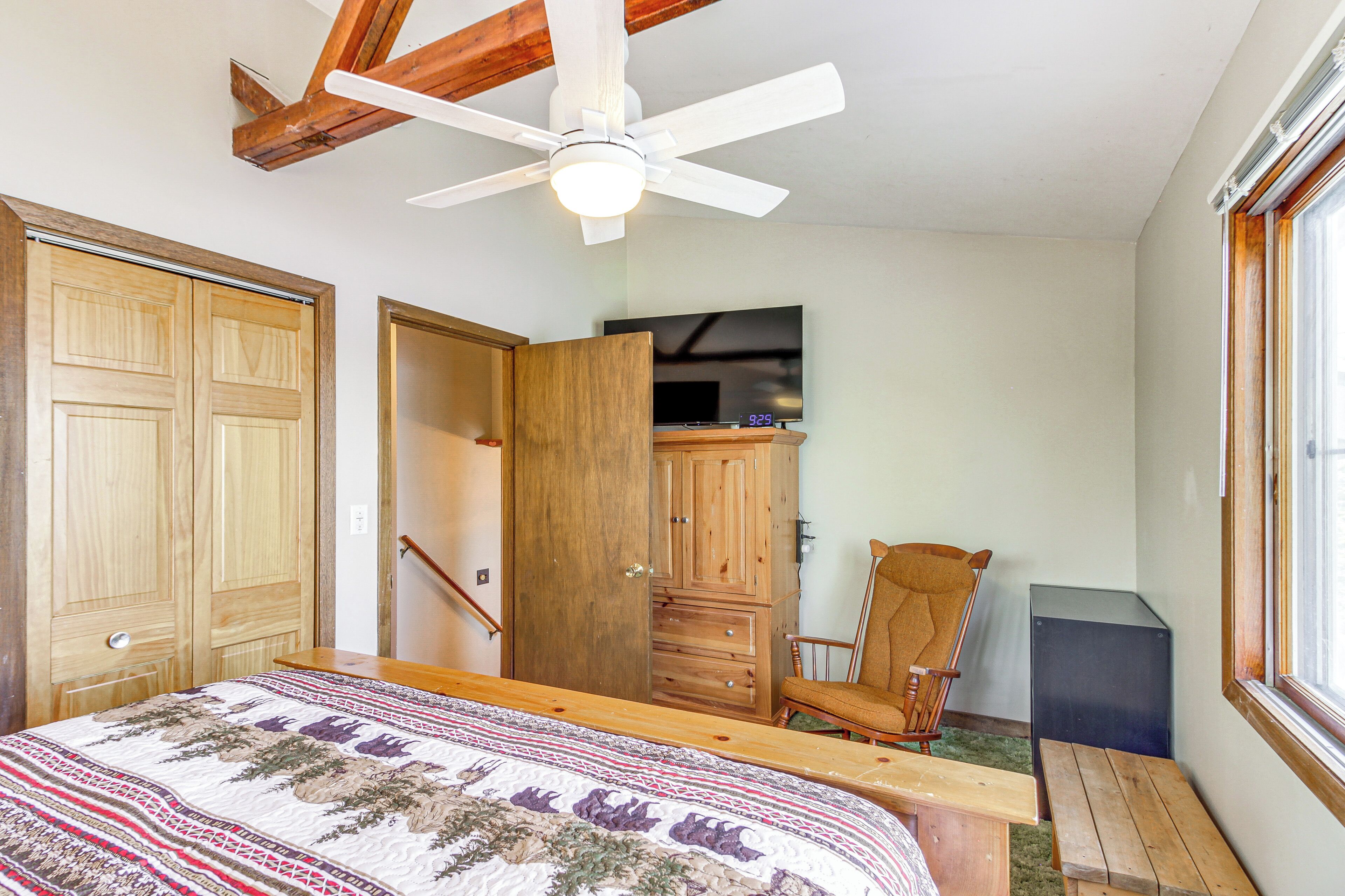 A bedroom with a bed, wooden wardrobe, a chair, a desk, and a ceiling fan.