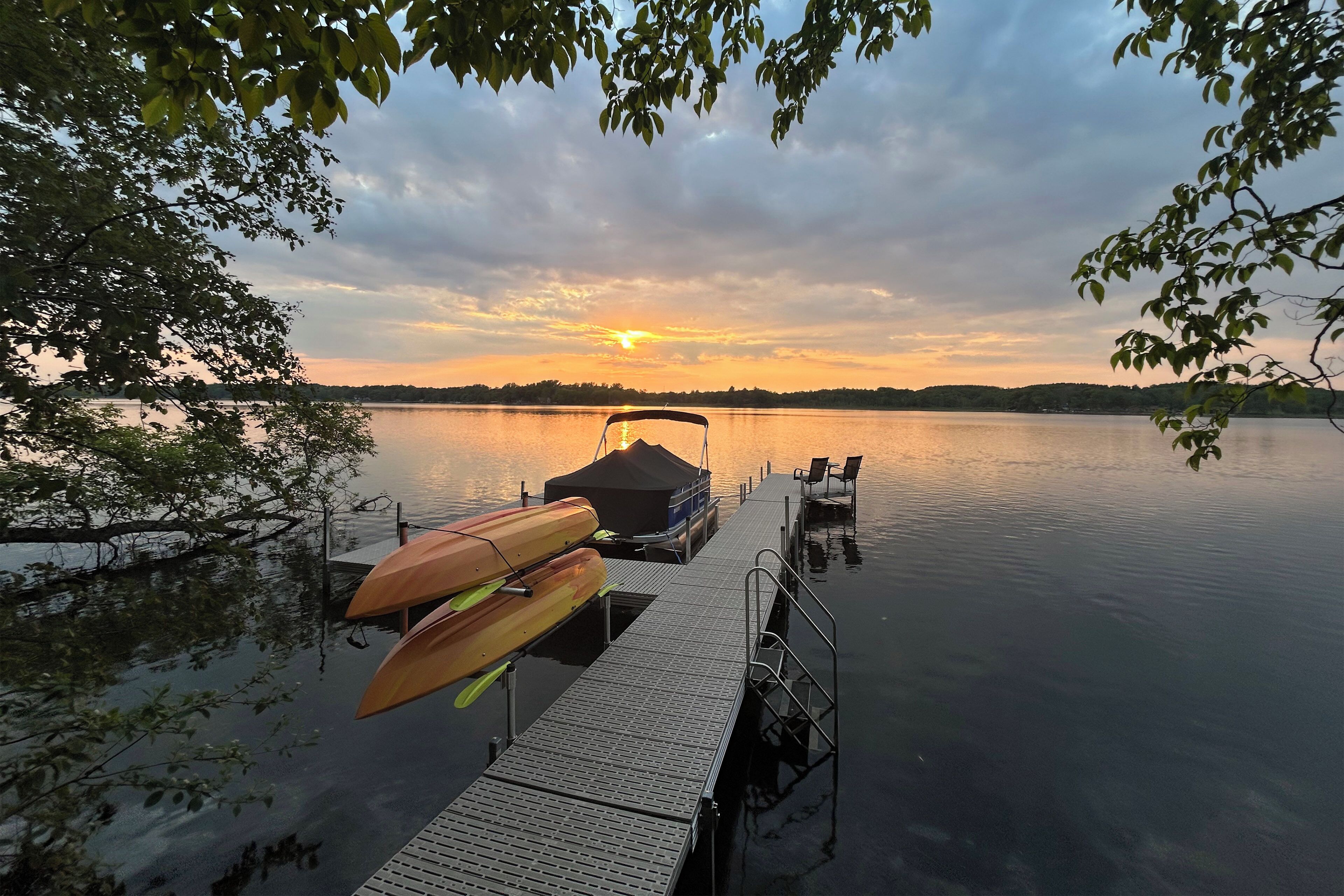 Un quai avec un bateau à l’abri et un canoë, un lac paisible et un coucher de soleil en arrière-plan.