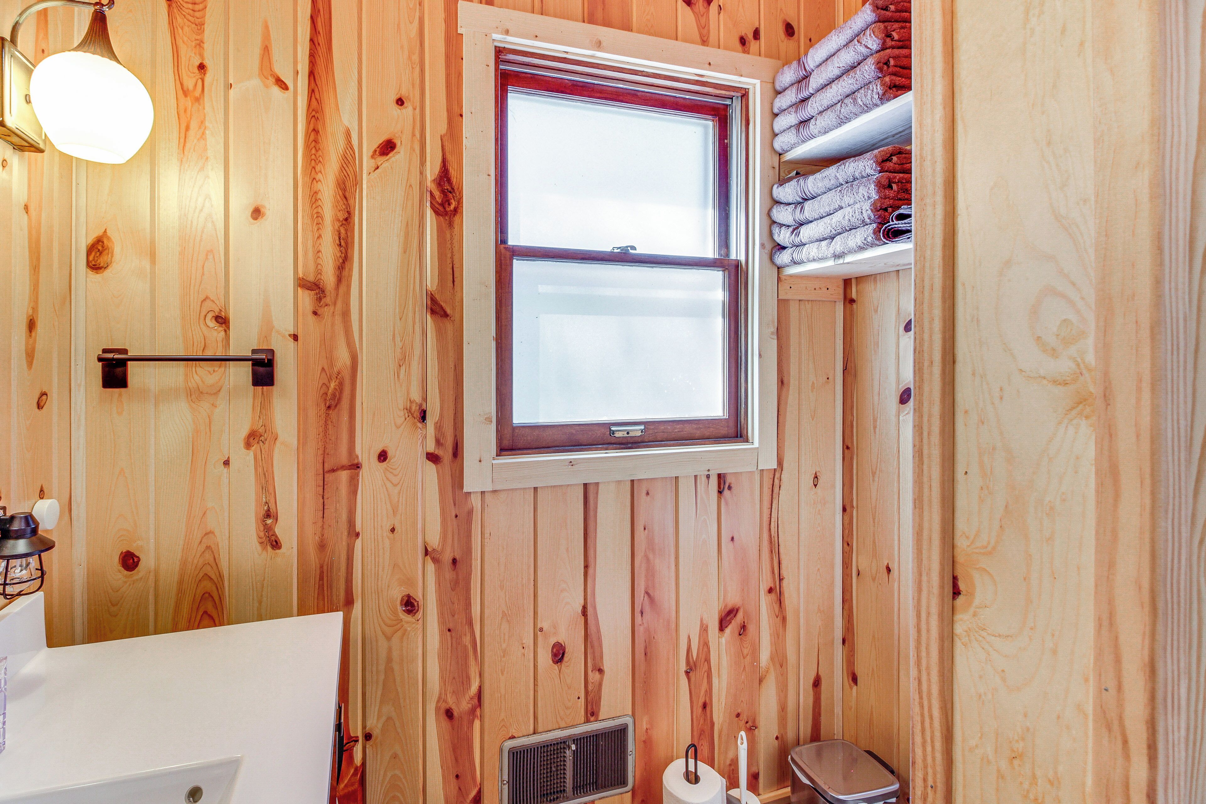 A wooden-paneled bathroom with a window, a towel rack, and a toilet.