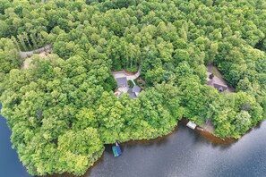 An aerial view of a forested island with a small dock and a boat. - Lakefront Roxboro Home w/ Private Dock! (Roxboro)