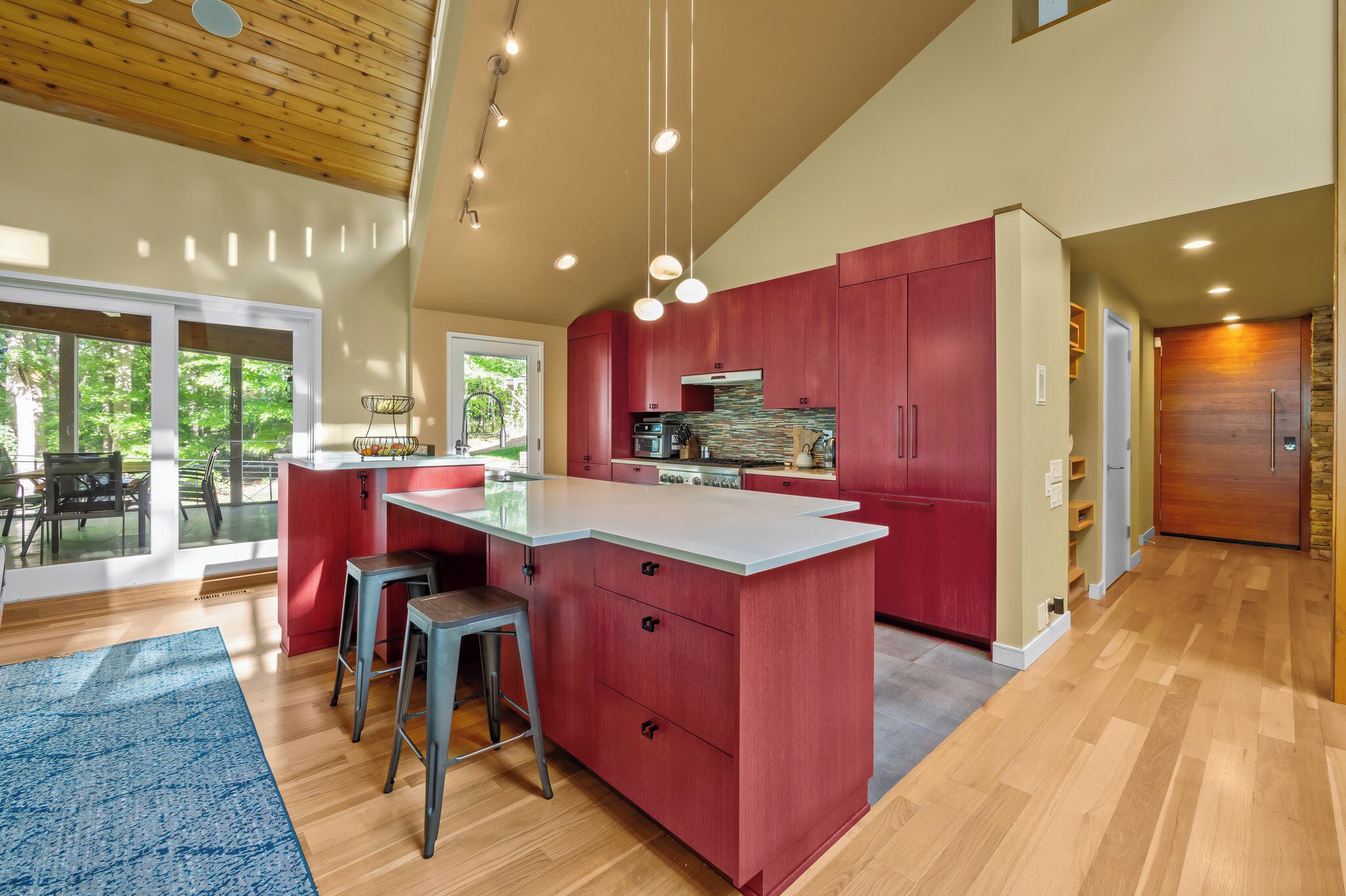 A modern kitchen with a central island, red cabinetry, and a large window.