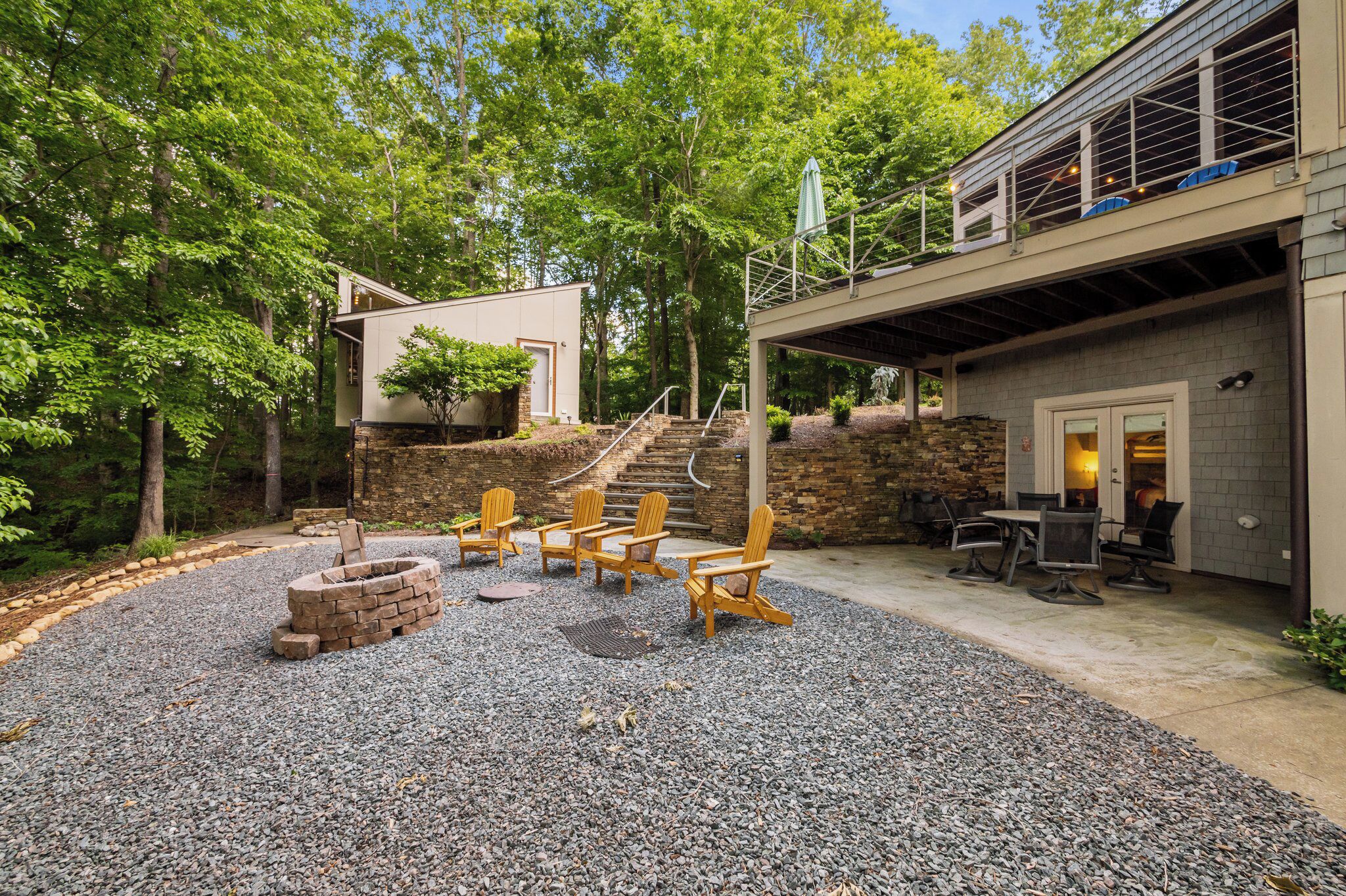 Un espace extérieur aménagé en terrasse, avec un foyer en pierre, des fauteuils Adirondack et un coin salon couvert équipé de tables et de chaises.