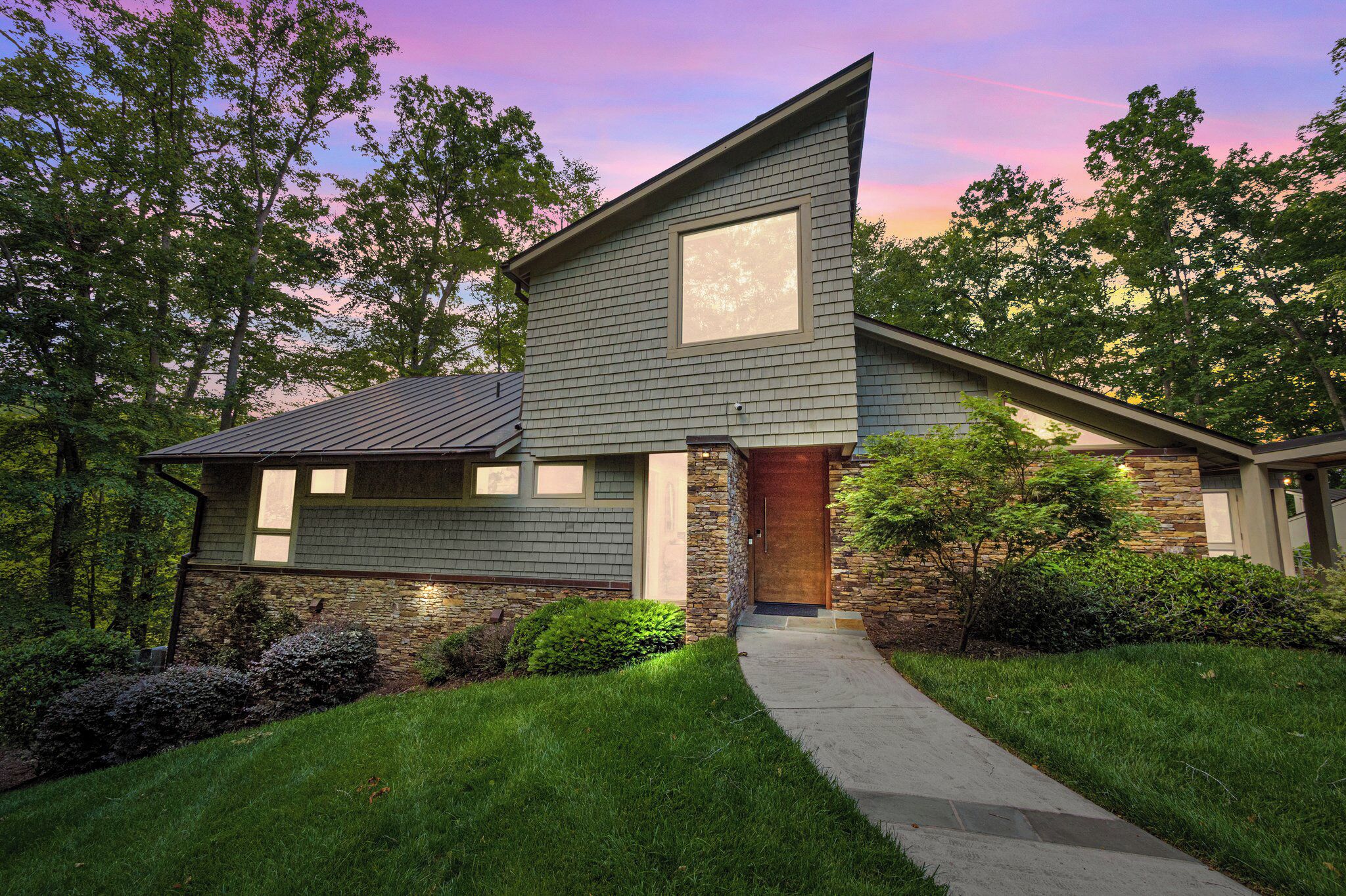 A modern two-story house with a stone foundation, a large front window, and a well-maintained lawn.