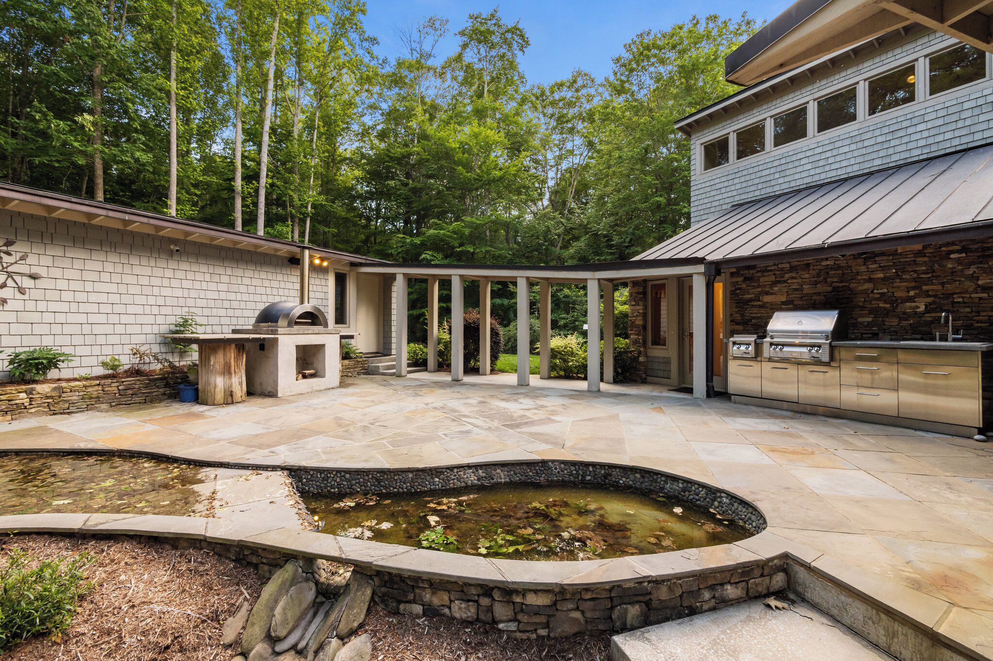 A backyard with a stone fire pit, a grill, and a pond.
