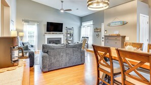 A living room with a gray sofa, wooden dining table, and chairs. There is a fireplace, a ceiling fan, and a sign that says "BEACH HOUSE". - Wilmington Family Home: 6 Mi to Wrightsville Beach (Wilmington)