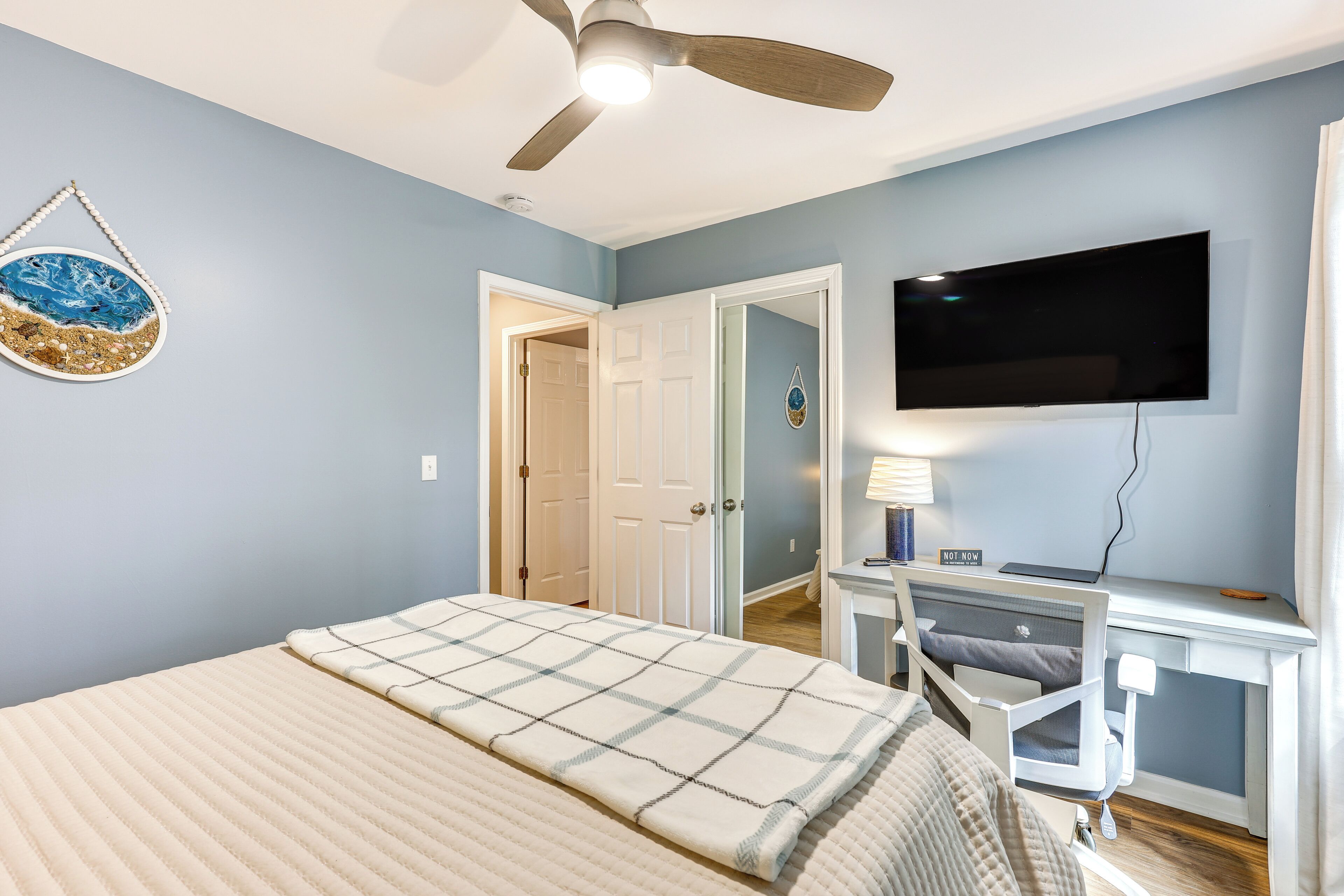 A bedroom with a bed, a desk with a computer, a TV, and a ceiling fan.