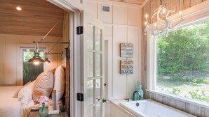 Ein Zimmer mit einem Bett, einem Fenster mit Blick auf Grünflächen, einer Badewanne und einem Kronleuchter.