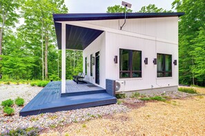 A modern cabin with a covered deck, large windows, and a flagpole.